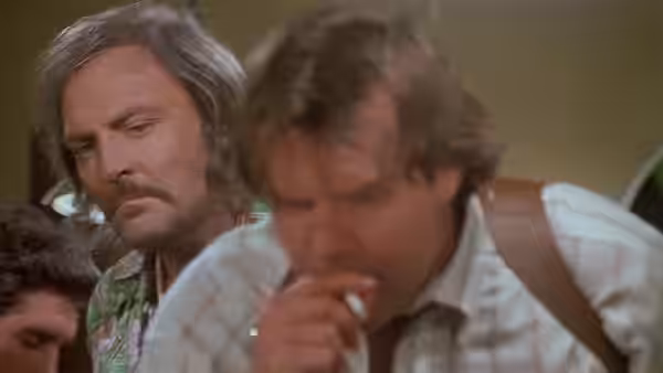 A gray-haired man watches as another man smokes beside him