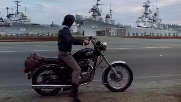 Zack Mayo (Richard Gere) sits astride his motorcycle beside docked Navy ships