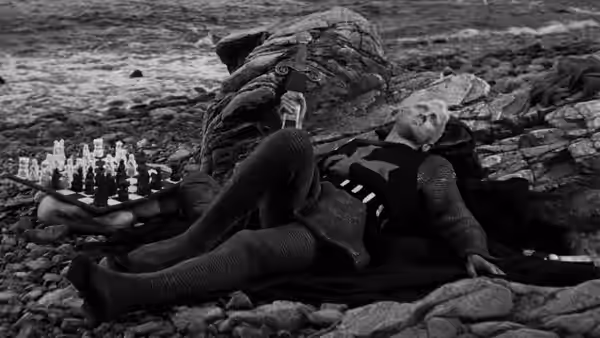 Antonius Block reclining on rocky shore beside chessboard