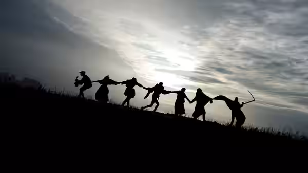 Silhouetted figures holding hands in a line on a hillside