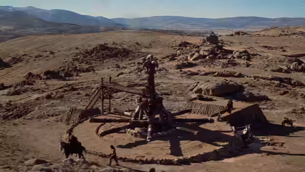 A small settlement and wooden structure stand in a vast desert landscape