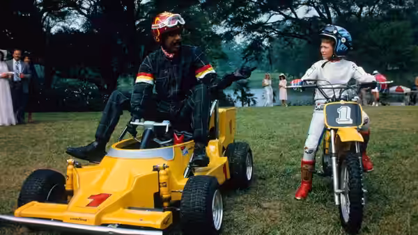 Jack Brown (Richard Pryor) rides a yellow go-kart beside Eric Bates on a dirt bike