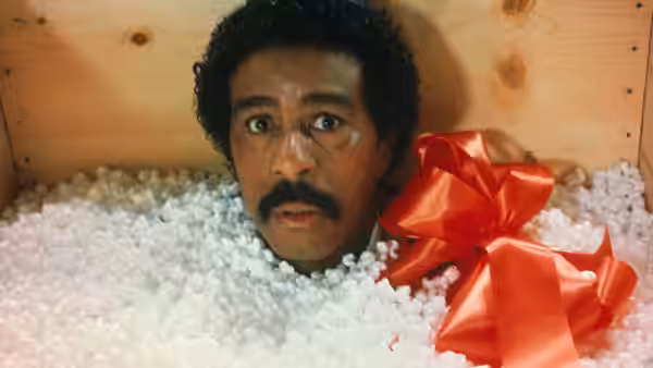 Jack Brown (Richard Pryor) lies buried in packing peanuts beside a large red bow