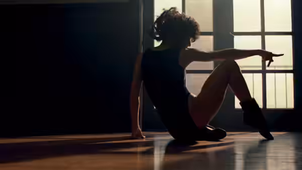 Alex Owens (Jennifer Beals) sits on a studio floor, pointing toward the window