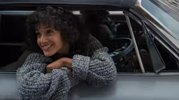 Alex Owens (Jennifer Beals) leans smiling over the open window of a car