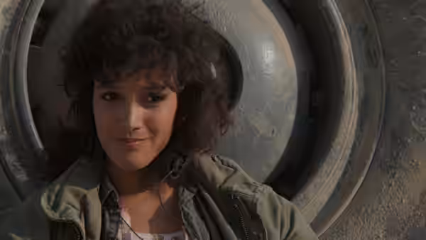 Alex Owens (Jennifer Beals) smiles beneath a large industrial metal wheel