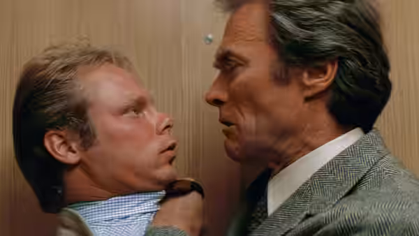 Harry Callahan (Clint Eastwood) grabs a man by the collar against a wooden door
