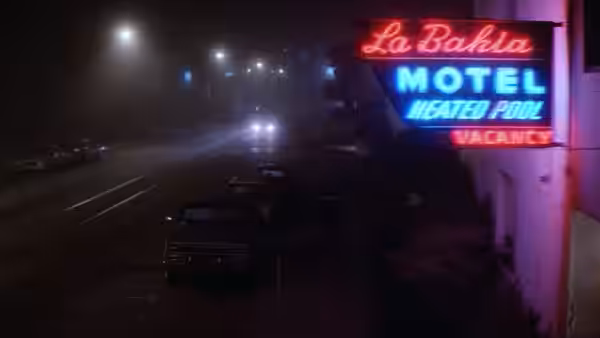 Cars pass a roadside motel with a neon vacancy sign