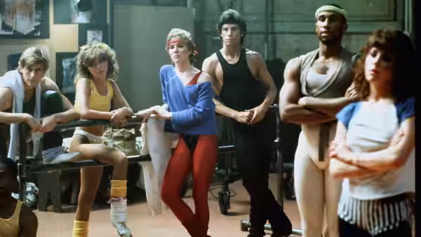 Tony Manero and Jackie watch dancers gathered in a rehearsal studio