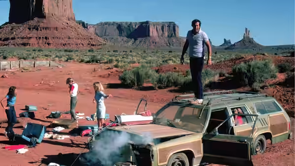 Clark Griswold (Chevy Chase) stands atop the smoking family station wagon in a desert campsite