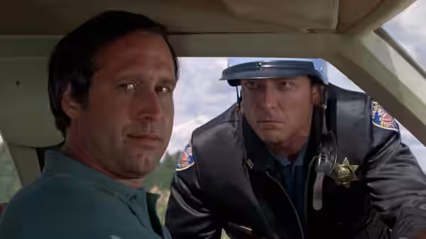 Clark Griswold sits beside a motorcycle cop leaning into the car window