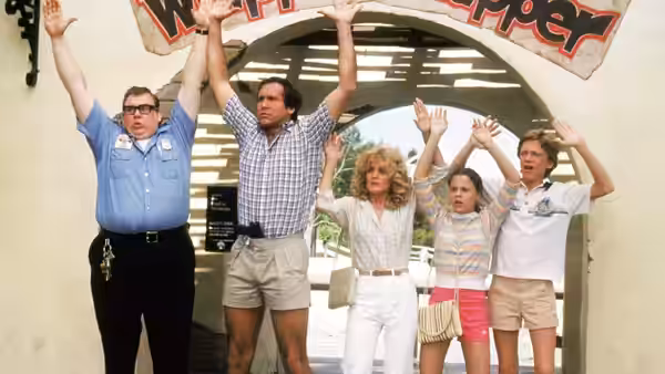 The Griswold family and a uniformed attendant raise their arms beneath a theme park entrance