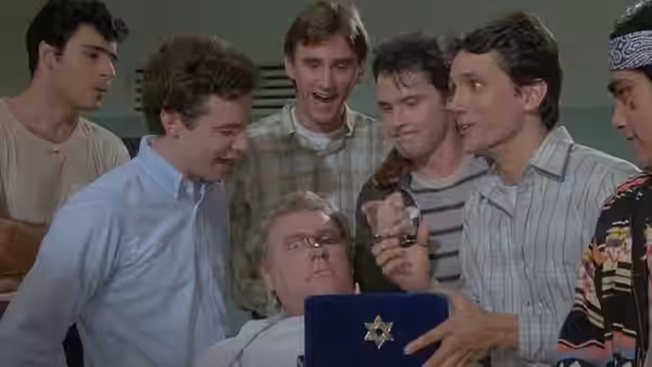 Several young men crowd around an older man holding a blue book and sheriff's badge