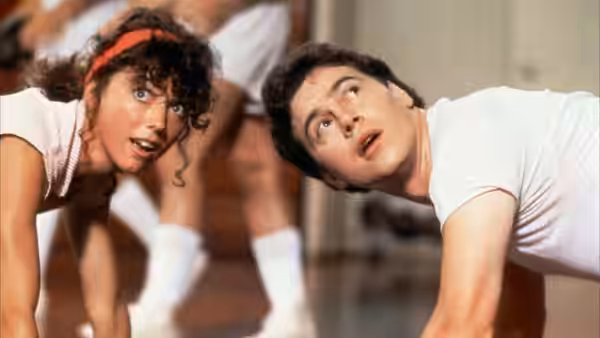 A young woman and man crouch low, both looking upward in a crowded room