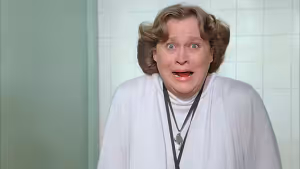 Balbricker (Nancy Parsons) stares wide-eyed in a white cardigan and pendant