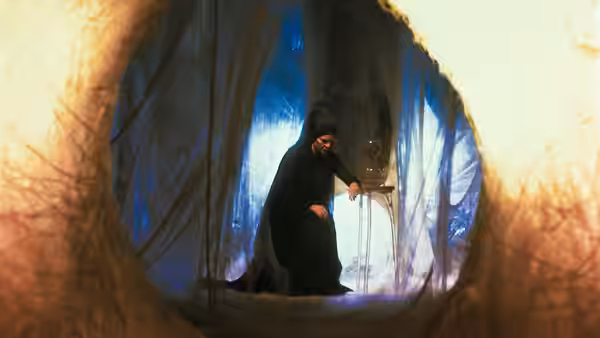 A cloaked figure stands with a staff inside a web-lined cavern