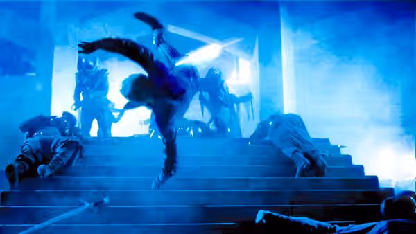 A man tumbles down broad stairs as fallen figures and armed attackers fill the blue-lit hall