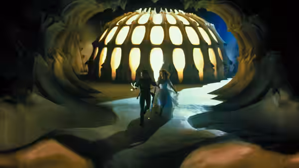 A man and woman enter a vast domed chamber through an organic, tunnel-like doorway