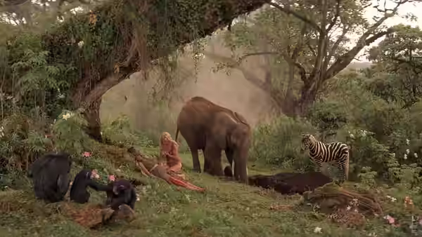 Sheena sits beneath a tree among an elephant, zebra, and other wild animals