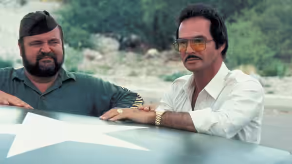 J.J. McClure (Burt Reynolds) stands beside a bearded man, both leaning against a vehicle