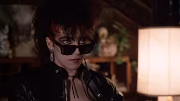 A woman in sunglasses and a leather jacket looks ahead indoors