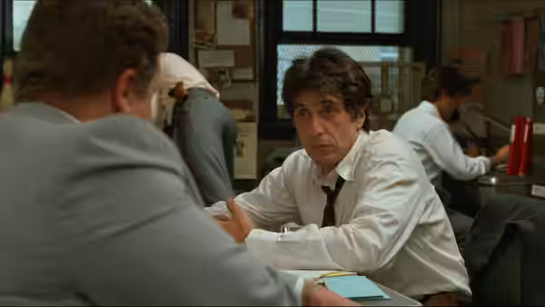 Frank Keller (Al Pacino) talks with a colleague across a desk at the police station