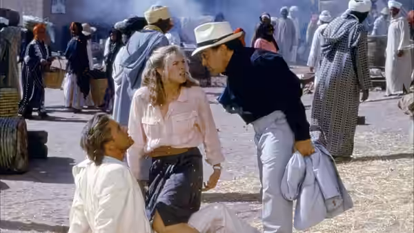 Joan Wilder stands between a kneeling man and a stranger leaning close in a crowded market