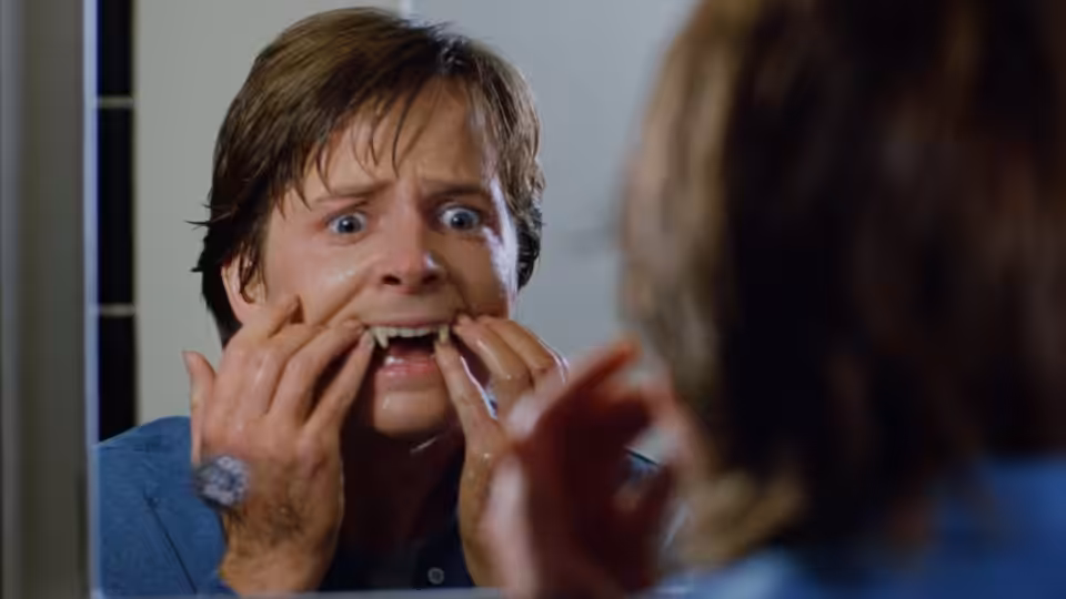 Scott Howard (Michael J. Fox) examines his teeth in a mirror, startled by his reflection