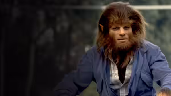 Scott Howard (Michael J. Fox), transformed into a werewolf, sits outdoors in a blue jacket