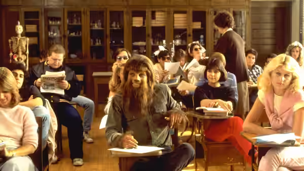 Scott Howard (Michael J. Fox), transformed into a werewolf, writes at a desk in a classroom