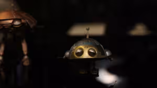 A small brass-colored hovering robot drifts through a dark room