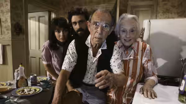 Frank Riley and Faye Riley lean forward with two younger residents in a crowded kitchen