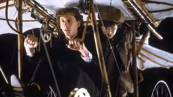 Sherlock Holmes (Nicholas Rowe) and John Watson (Alan Cox) crouch among ropes inside a wooden contraption