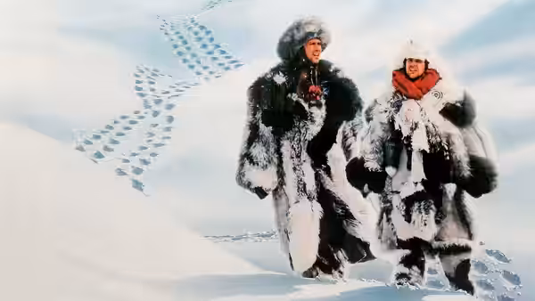 Emmett Fitz-Hume (Chevy Chase) and Austin Millbarge (Dan Aykroyd) trek across a snowy landscape in fur parkas