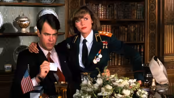 Emmett Fitz-Hume (Chevy Chase) sits at a desk as Karen Boyer (Donna Dixon) puts an arm around him