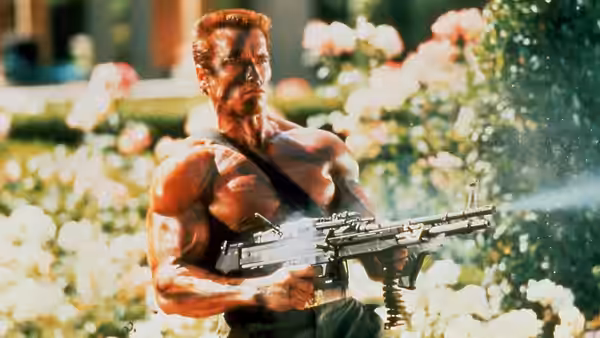 John Matrix (Arnold Schwarzenegger) carries a machine gun through a sunlit garden