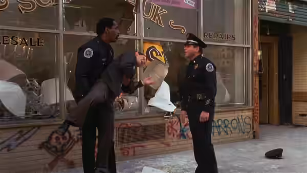 Two uniformed officers examine a vandalized storefront as debris covers the sidewalk