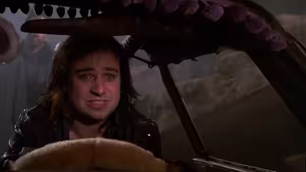 A long-haired man sits at the wheel beneath a large tentacled object