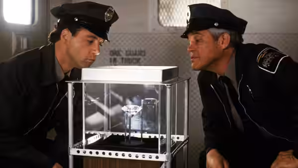 Two uniformed officers peer into a glass display case containing a small object