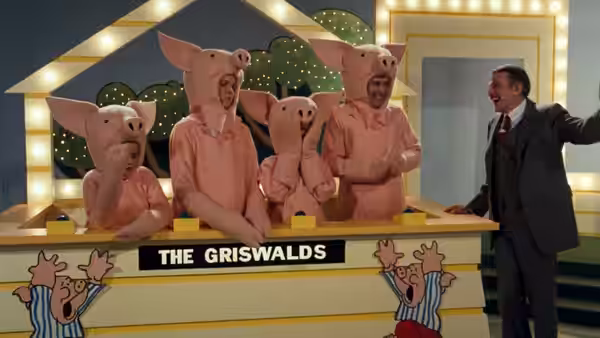 The Griswolds wear pig costumes behind a game-show podium as the host gestures