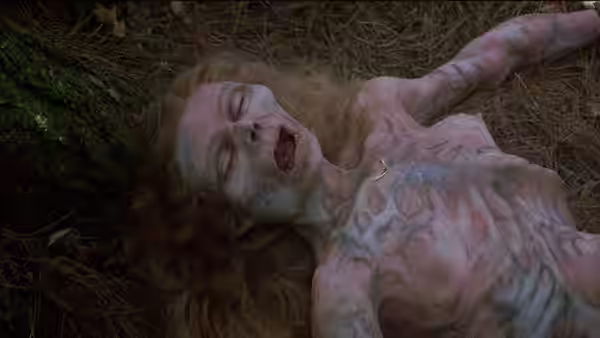 A pale, emaciated woman lies unconscious on the forest floor