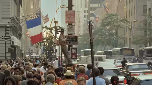 A crowded city street packed with pedestrians and traffic beneath hanging flags
