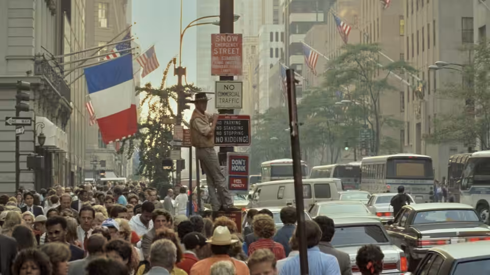 A crowded city street packed with pedestrians and traffic beneath hanging flags