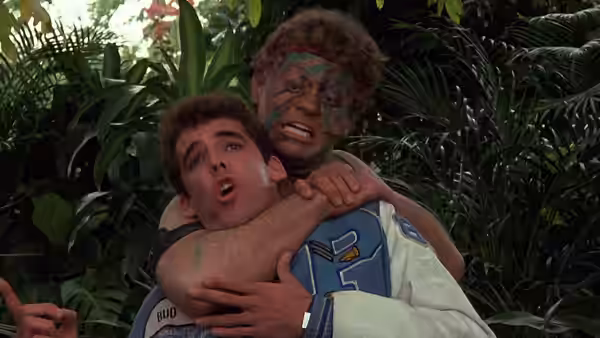 Carey Mahoney (Steve Guttenberg) struggles in a leafy garden as a painted cadet grabs him