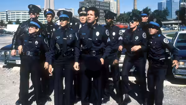 Police cadets in uniform gather beside parked cars on a city street