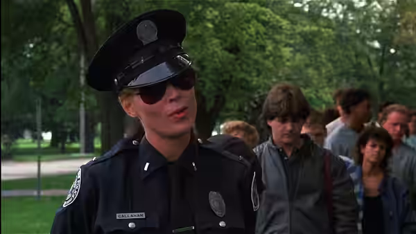 Cadet Zed (Bobcat Goldthwait) speaks to a group outdoors in a police uniform and sunglasses