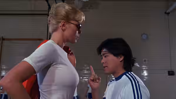 Lieutenant Callahan (Leslie Easterbrook) towers over a cadet in a gym as he raises one finger