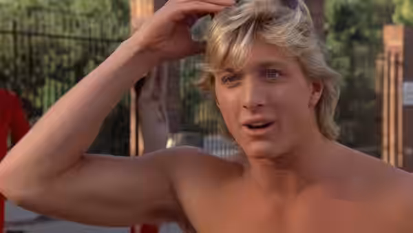 Chas (William Zabka) touches his hair while standing shirtless outdoors