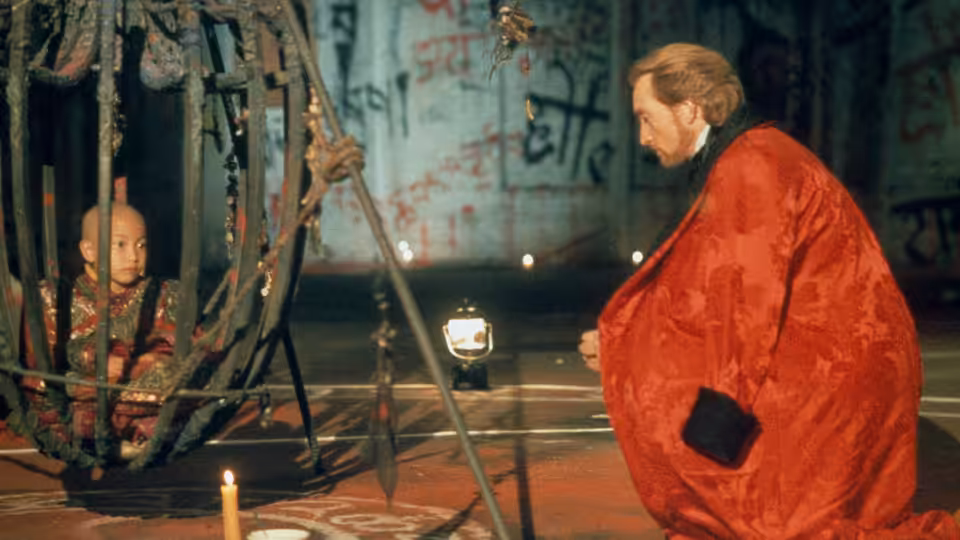 Sardo Numspa (Charles Dance) kneels beside the Golden Child, imprisoned inside a metal cage