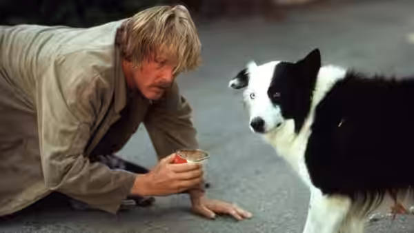 Jerry Baskin (Nick Nolte) crouches beside a black-and-white dog, holding a cup